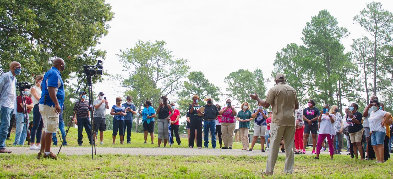 Pastor Demethrius Boyd of St. Paul Missionry Baptist Church in Mineola addresses the crowd gathered  Wednesday morning in the Cedar Memorial Gardens just east of the fence separating it from the Black cemetery.
